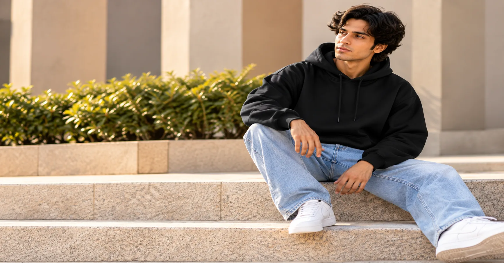 Man wearing a black hoodie with light-wash jeans and white sneakers for a casual everyday outfit